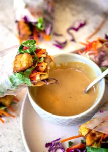 A vegetable salad roll being dipped in peanut sauce.
