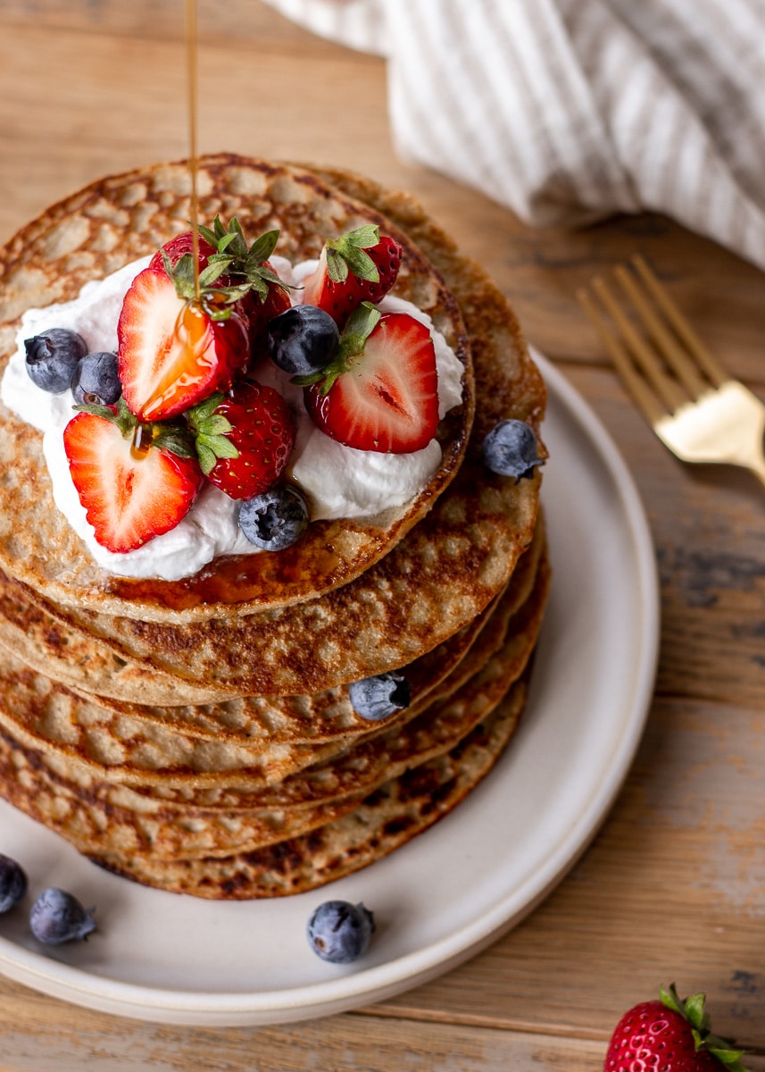 Closeup shot of a stack of 3 ingredient banana oatmeal pancakes topped with coconut whipped cream and berries.