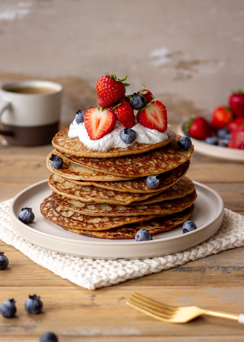 A stack of 3 ingredient banana oatmeal pancakes topped with coconut whipped cream and berries.