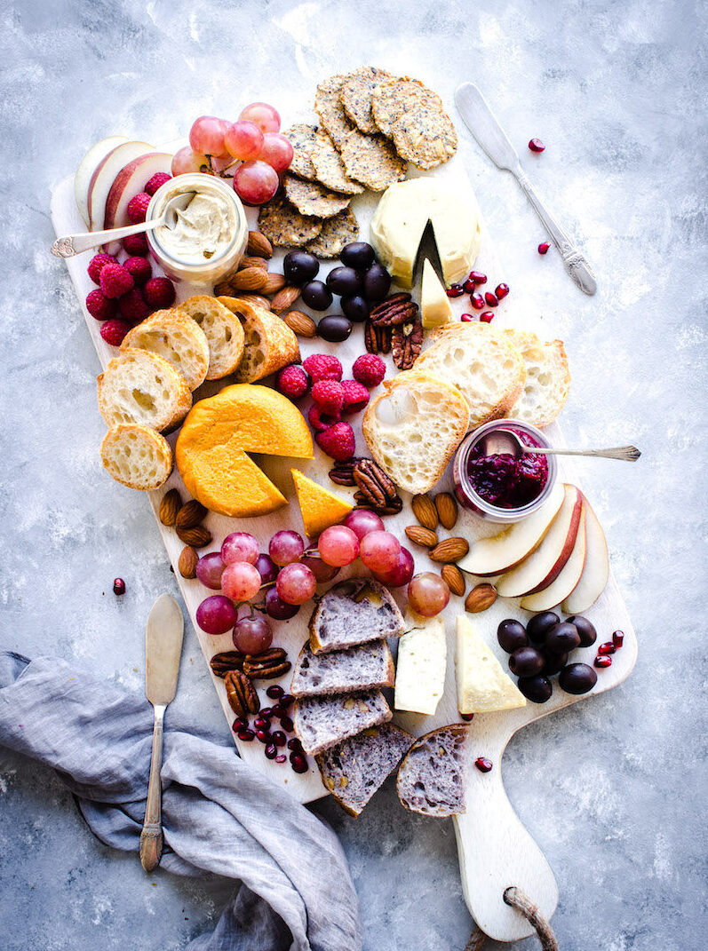 Vegan cheese board packed with cheese wheels, breads, crackers and grapes.