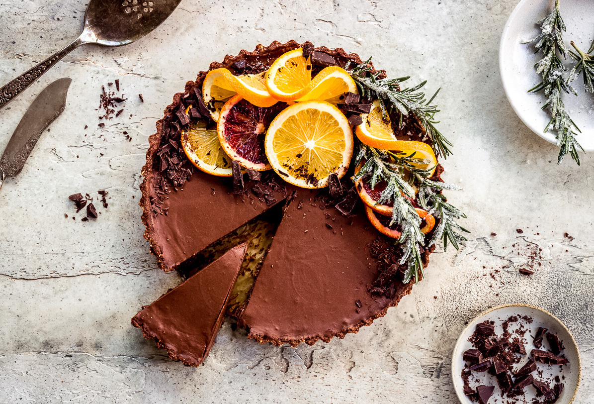 Overhead image of chocolate orange tart decorated with orange slices and rosemary.