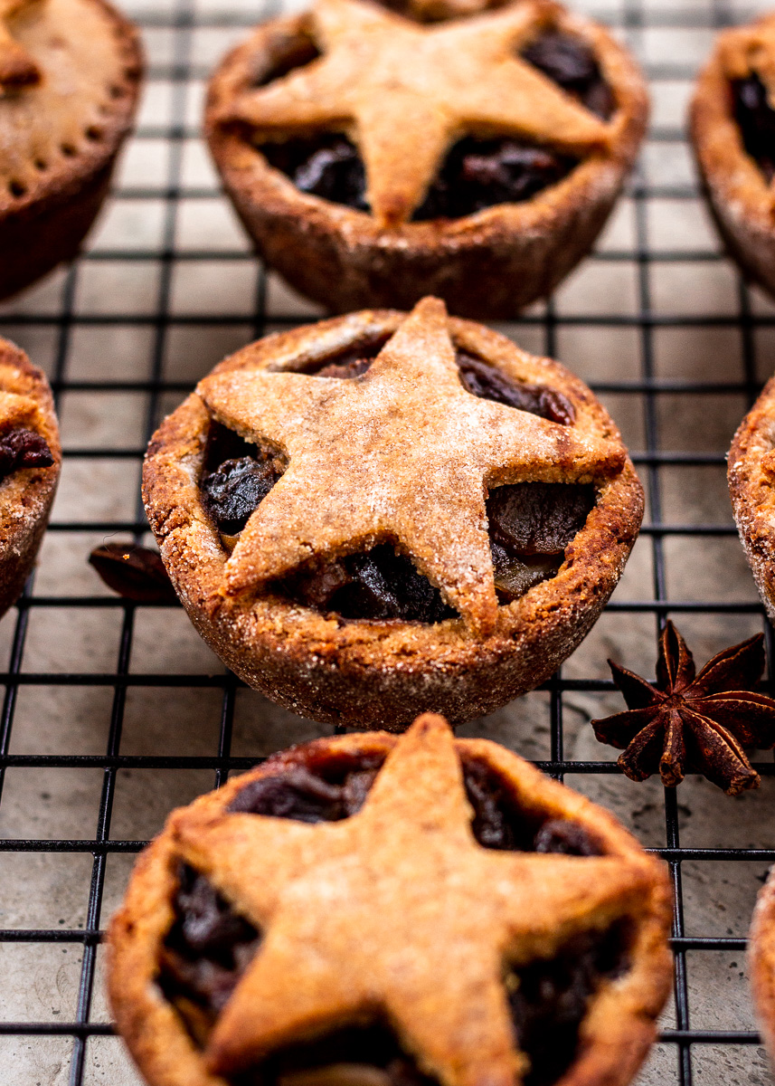 Festive mince pies with pastry stars on top cooling on rack.