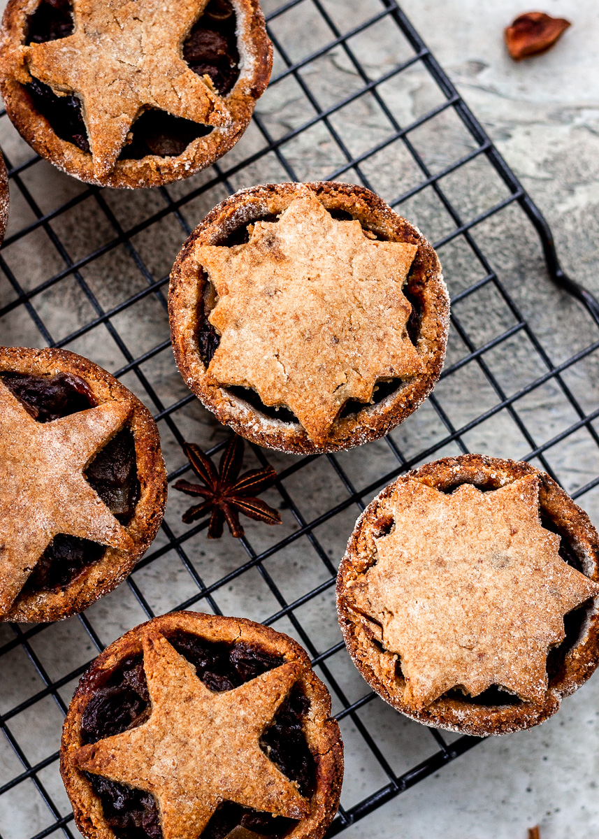 Festive mince pies with pastry stars on top cooling on rack.