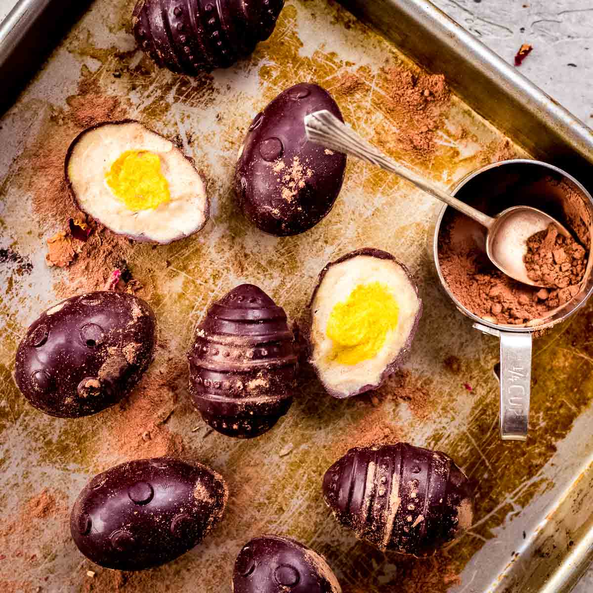 overhead image of homemade vegan creme eggs on a baking tray, with cocoa powder nearby in a cup.