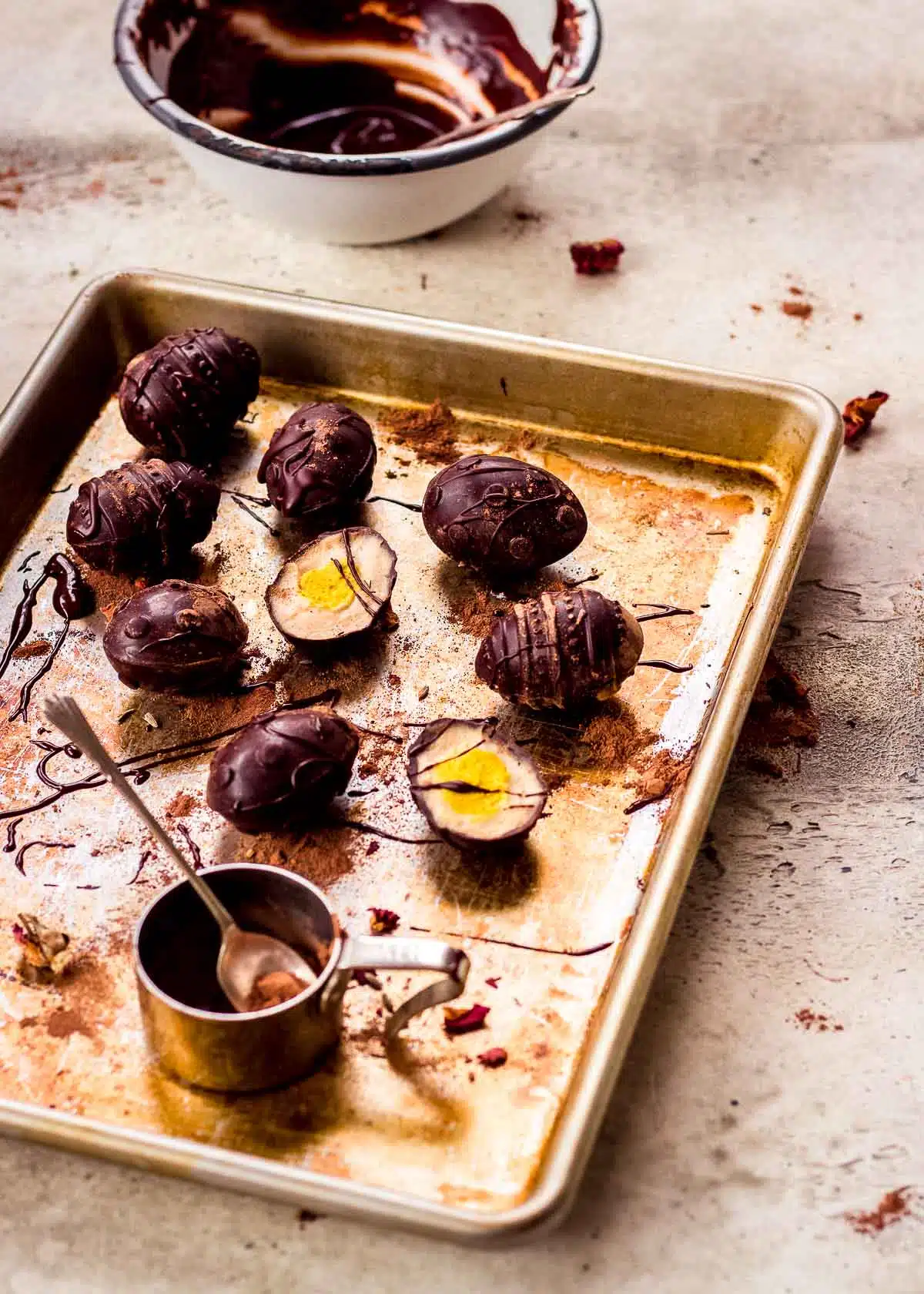 Vegan creme eggs on baking tray with bowl of melted chocolate.