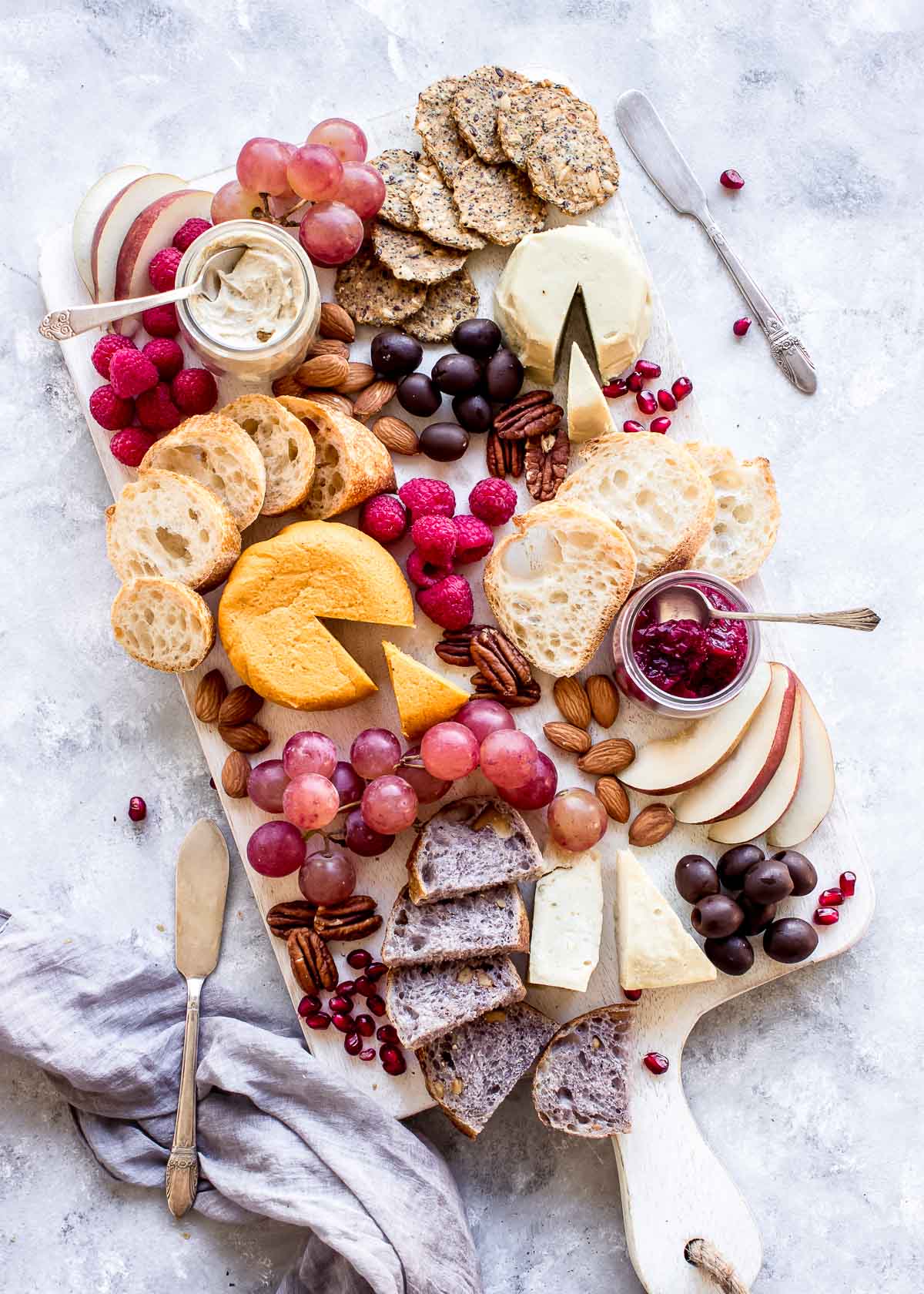 Vegan Cheese Board showing multiple hard cheeses, berries, bread and crackers.