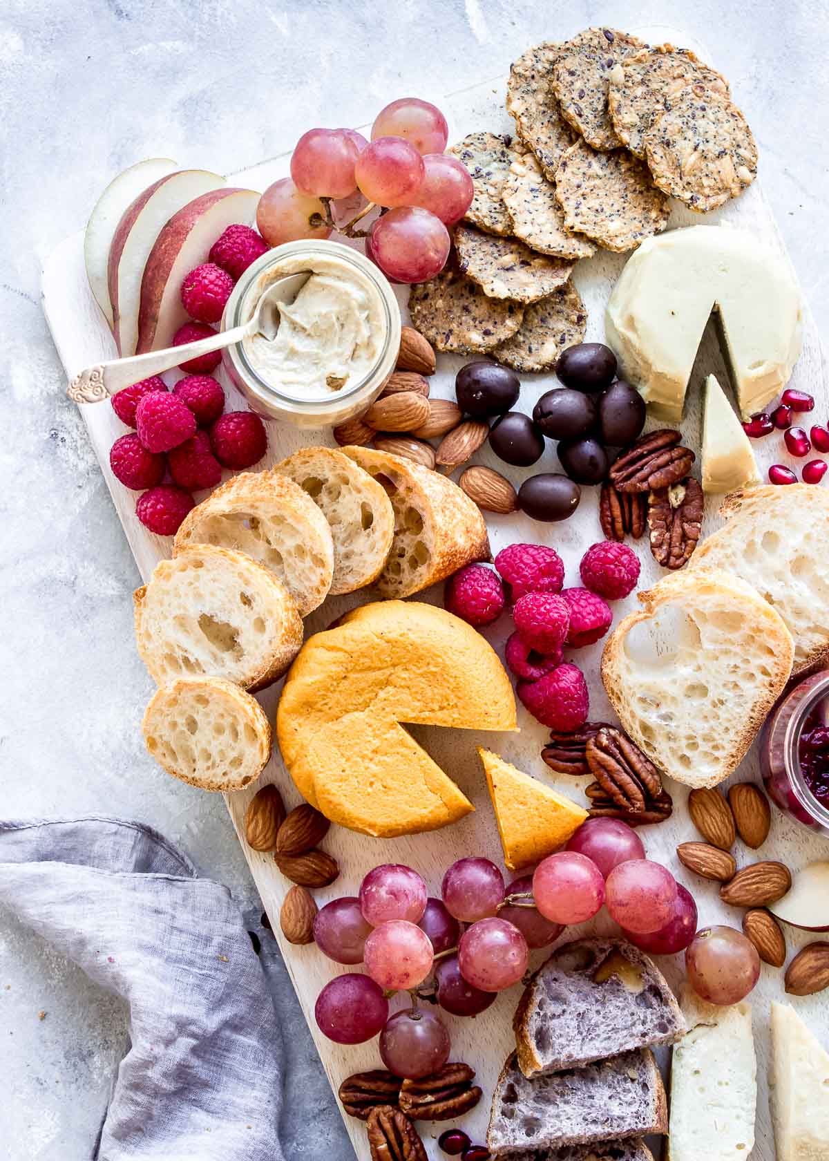 Vegan cheese board showing multiple hard cheeses, berries, bread and crackers.