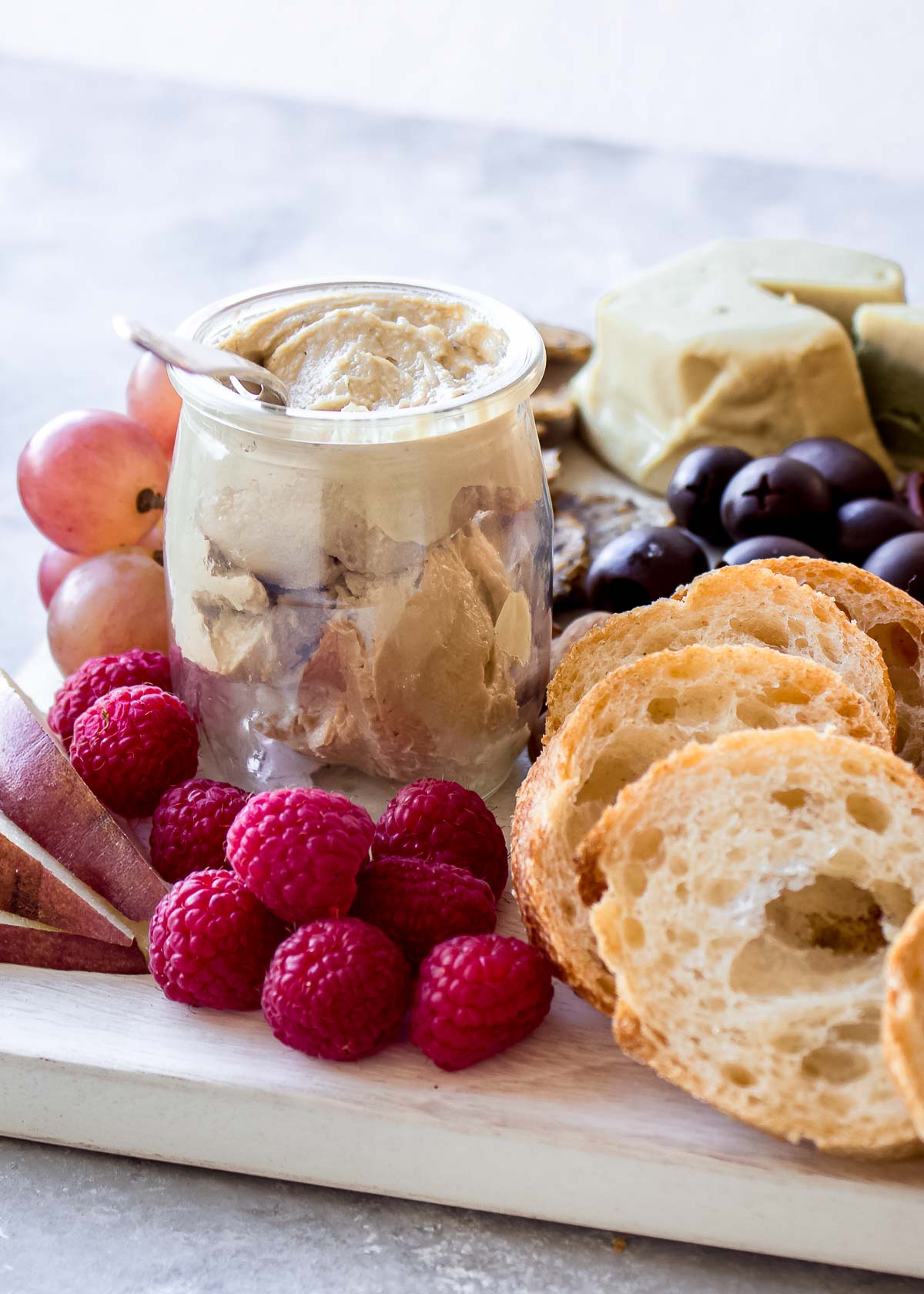 Section of vegan cheese board showing dip, artisan vegan cheese, bread, grapes and berries.
