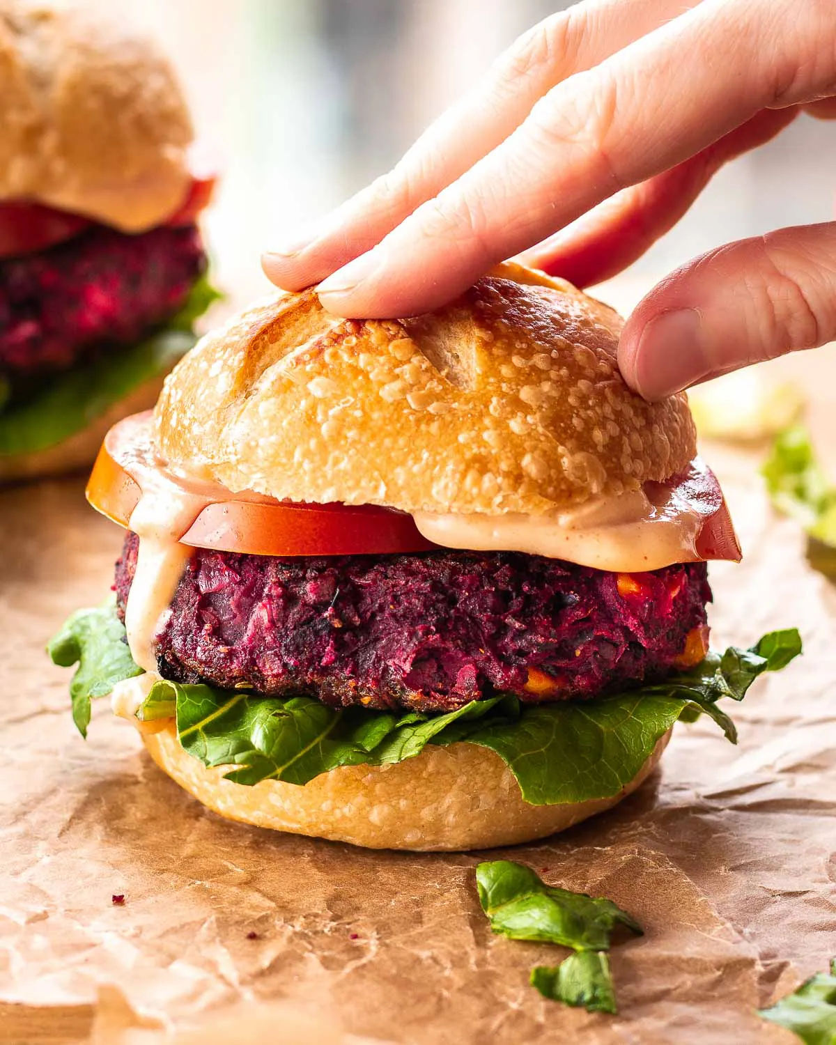 Woman's hand pressing down on beet and black bean burger in bun with mayo.