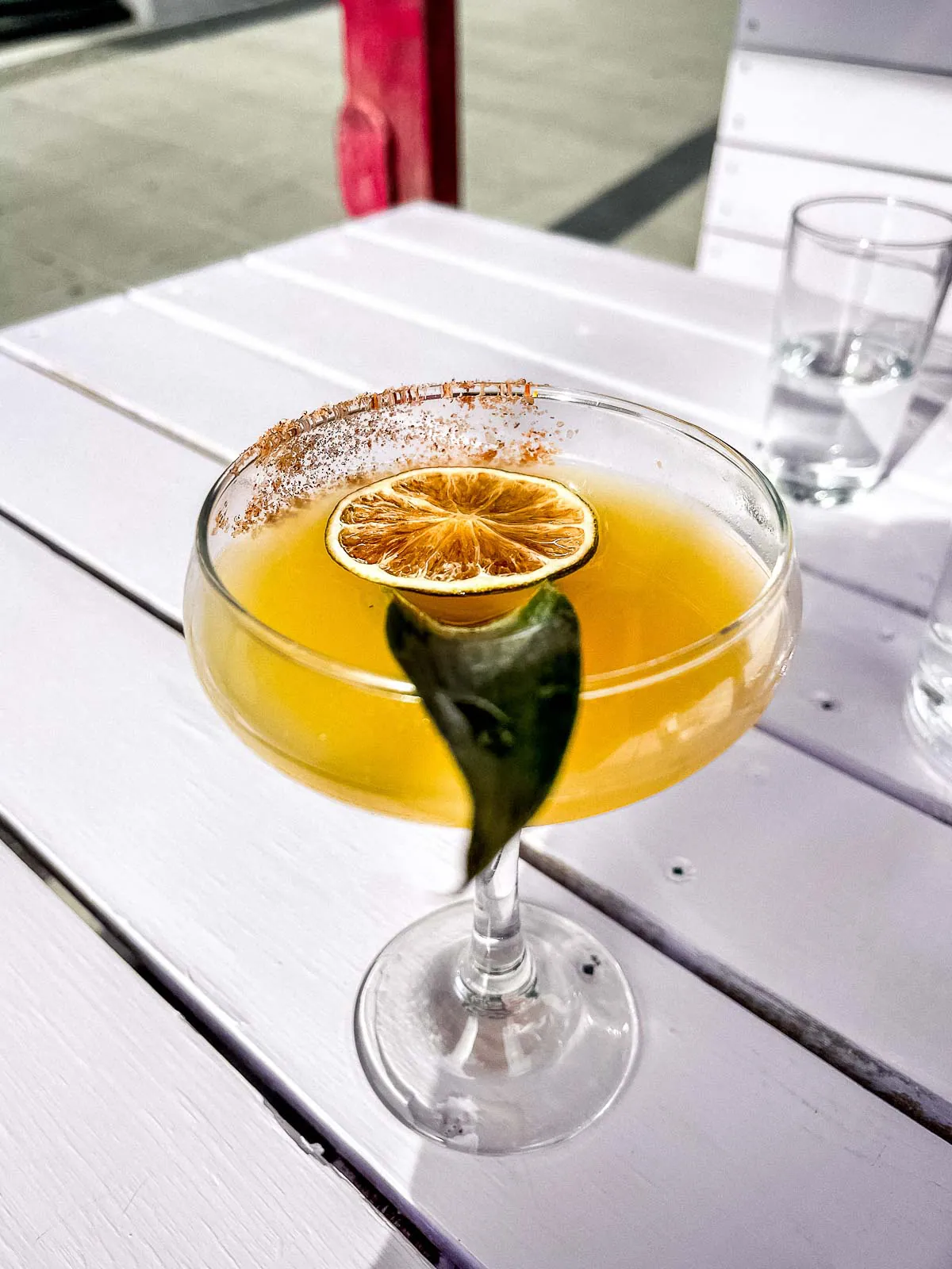 Yellow cocktail on sun-dappled table.