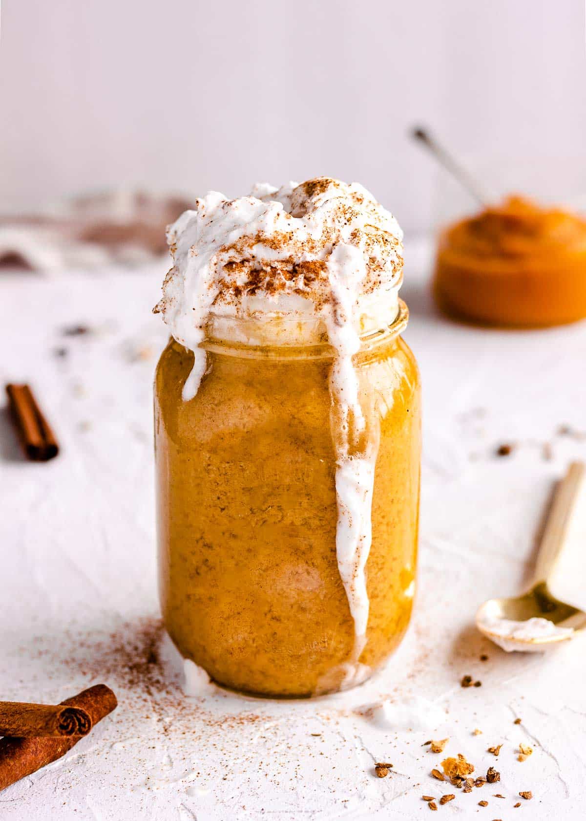 Iced pumpkin spice latte with whipped coconut cream dripping down the sides.