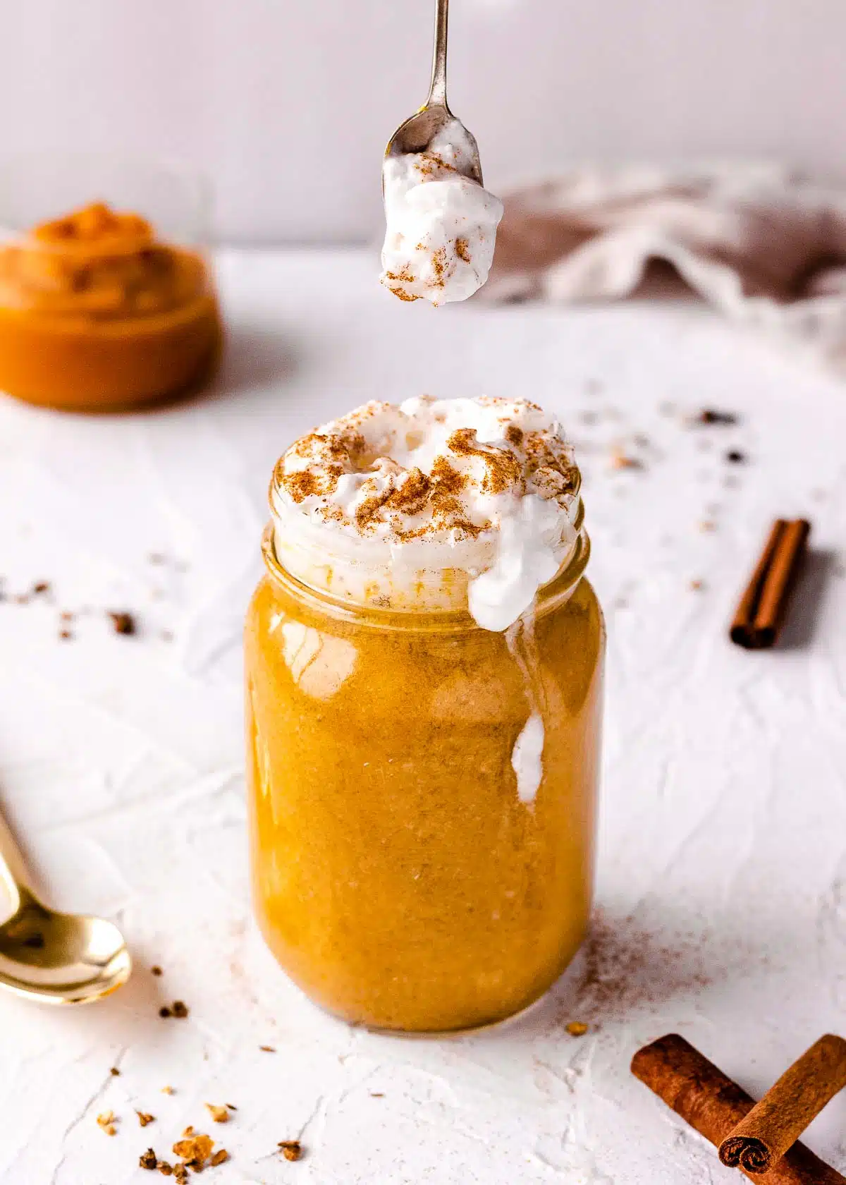 A spoon of coconut whipped cream hovers over a glass of iced pumpkin spice latte.