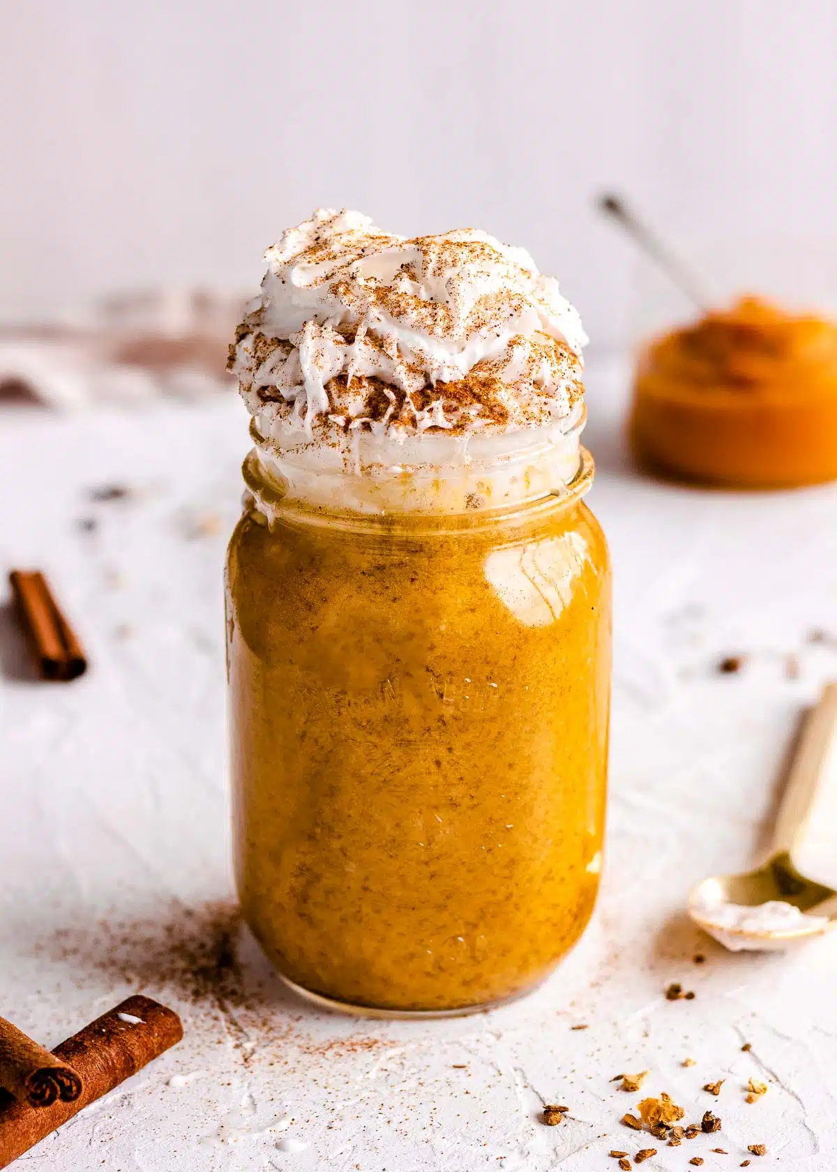 A tall glass jar of pumpkin latte topped with whipped coconut cream and cinnamon.