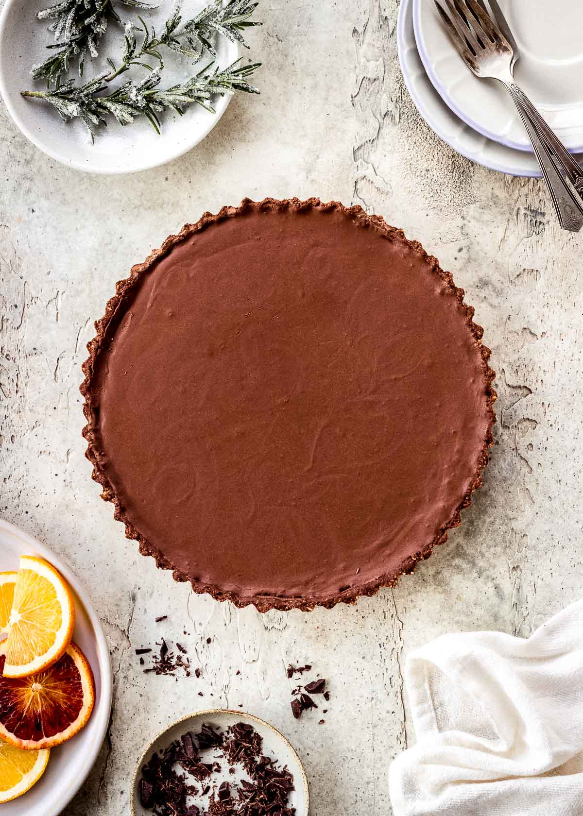 Plain chocolate ganache tart with chopped chocolate and rosemary sprigs nearby.