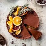 Vegan chocolate orange tart decorated with sprigs of rosemary and orange slices.