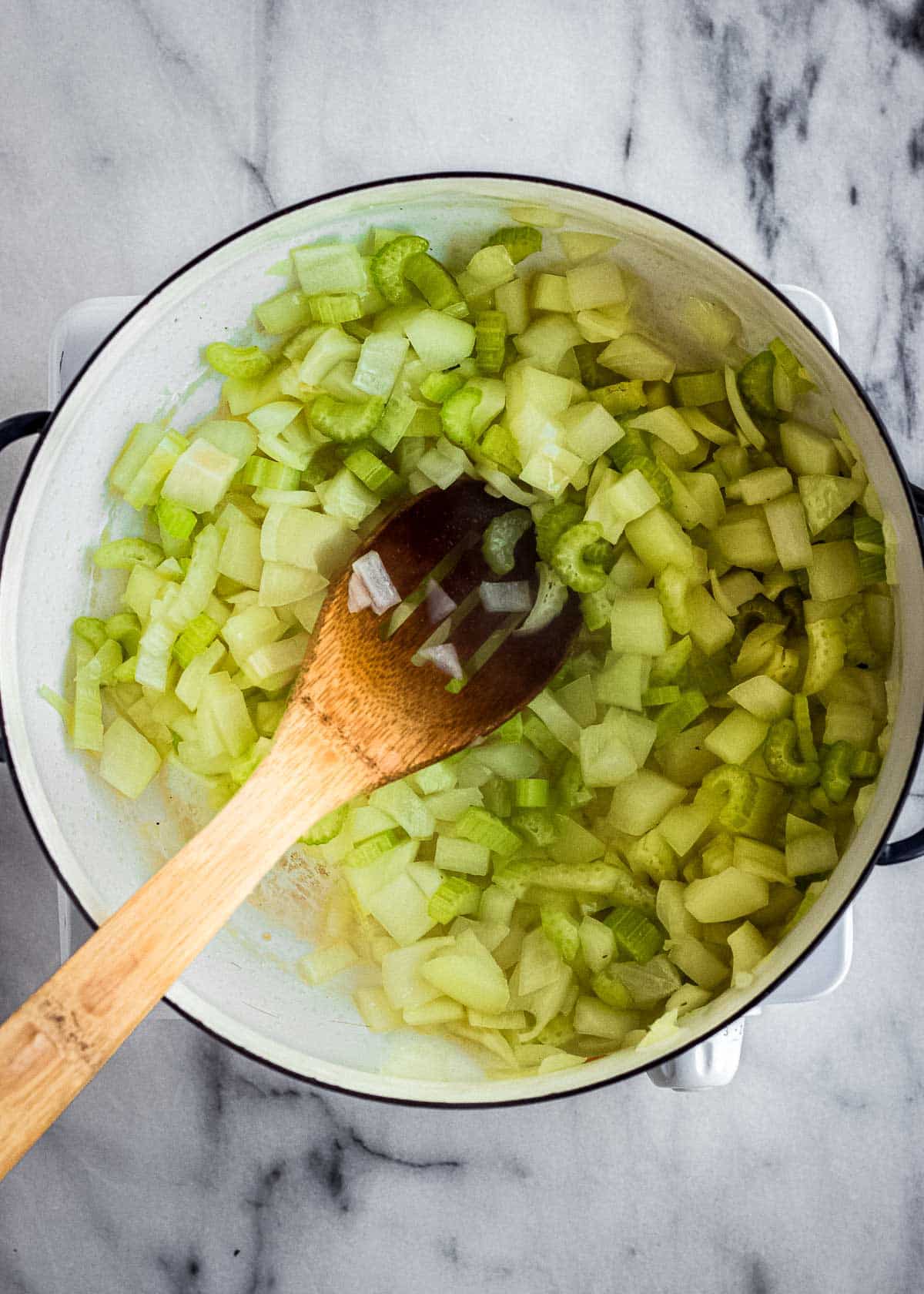 A large soup pot containing celery and onions sauteeing.