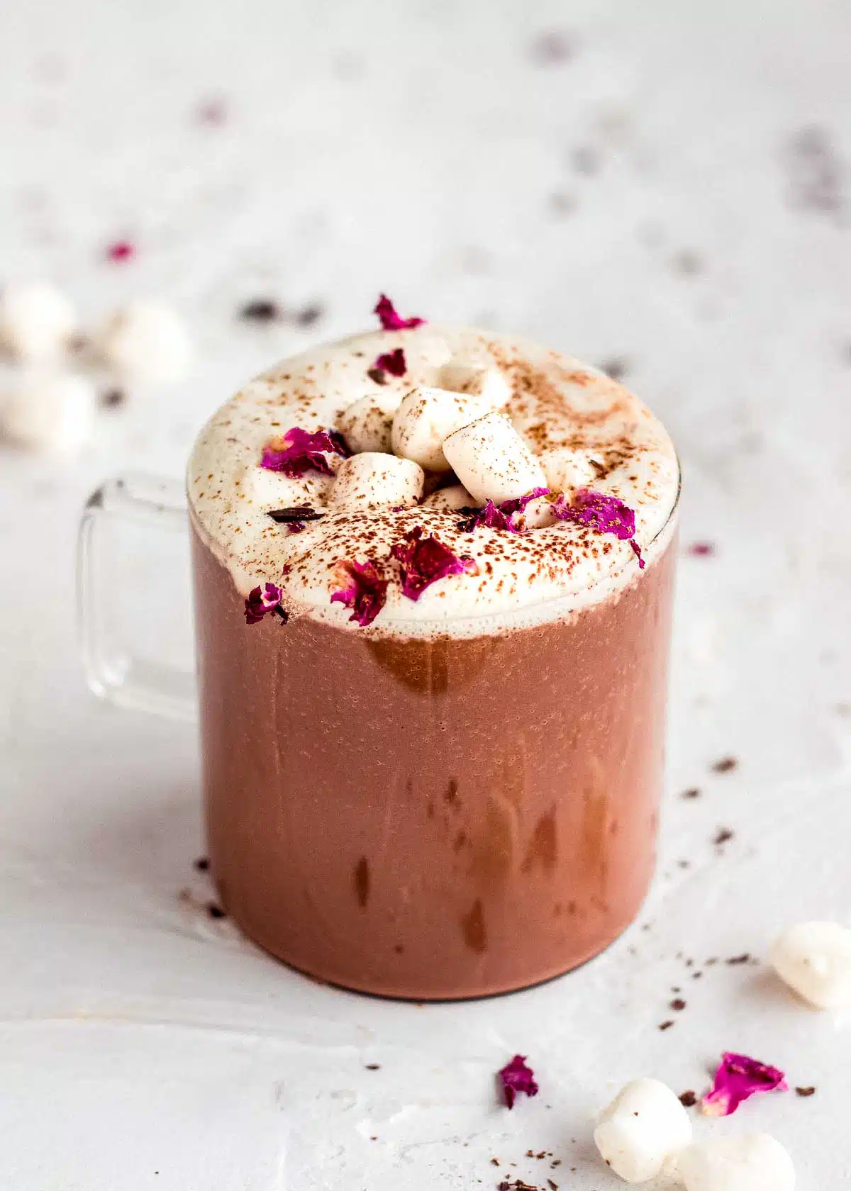 Glass mug of rose hot chocolate topped with whipped cream and marshmallows.