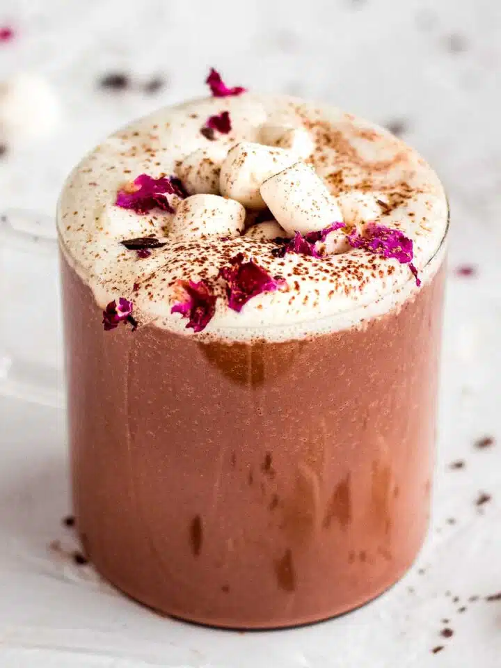 Glass mug of rose hot chocolate topped with whipped cream, rose petals and marshmallows.