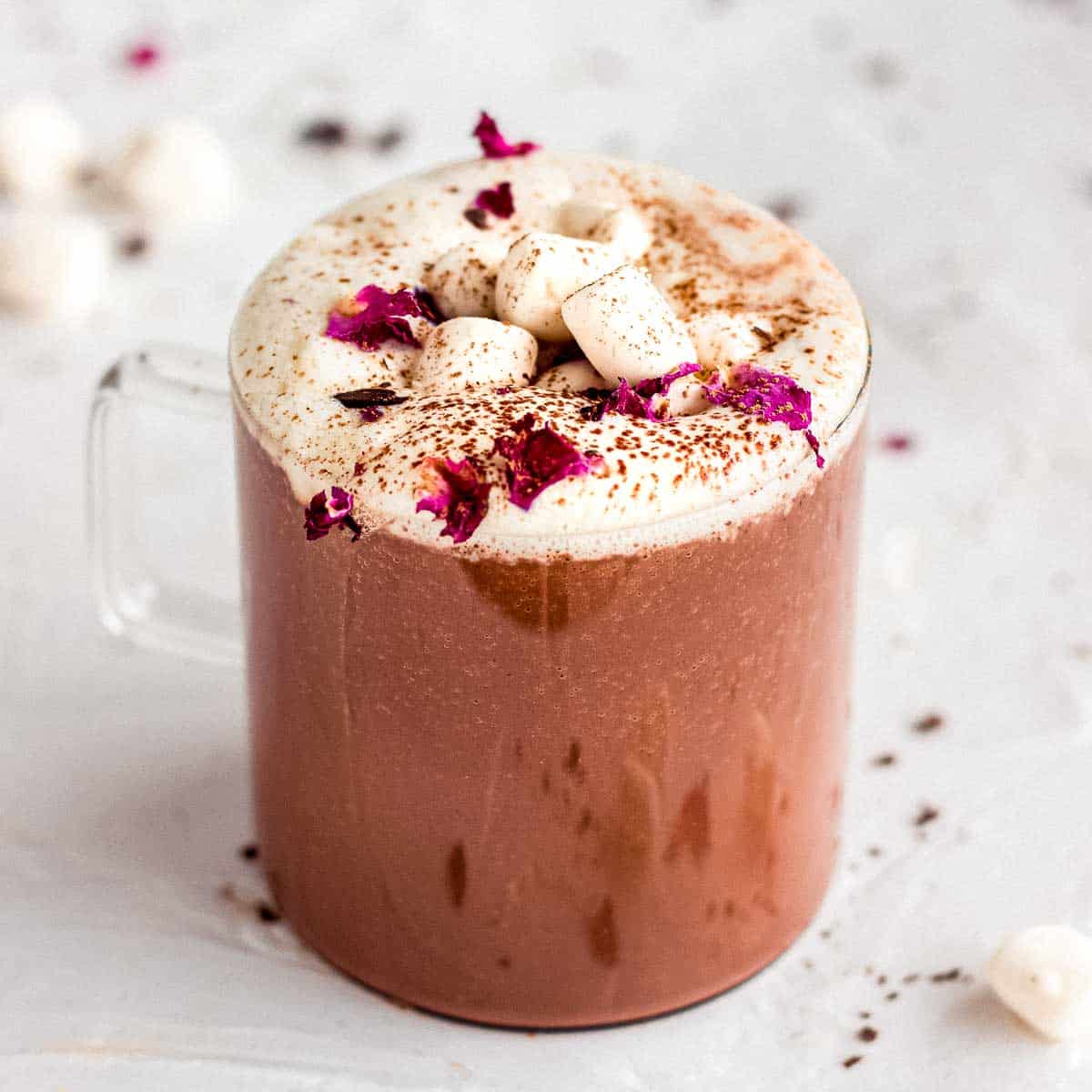 Glass mug of rose hot chocolate, topped with marshmallows and rose petals.