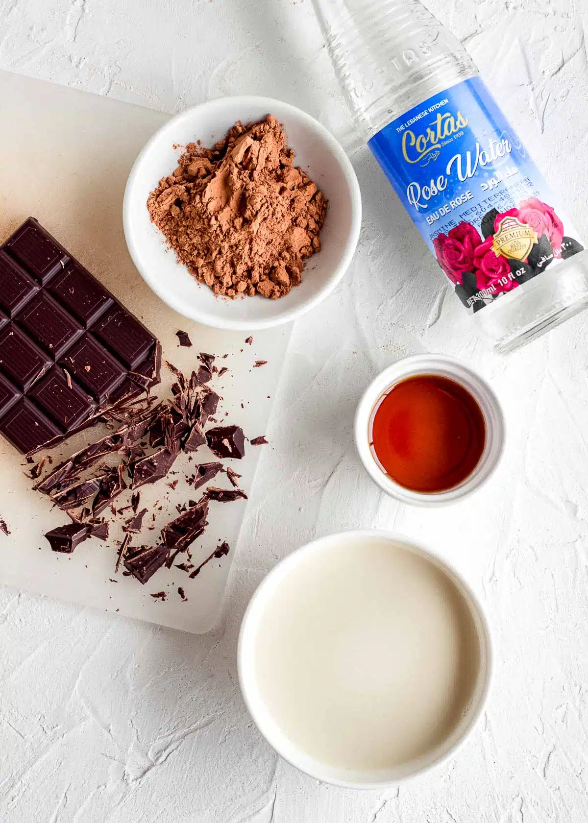 Ingredients to make rose hot chocolate: dark chocolate, cocoa powder, rose water, maple syrup and milk.