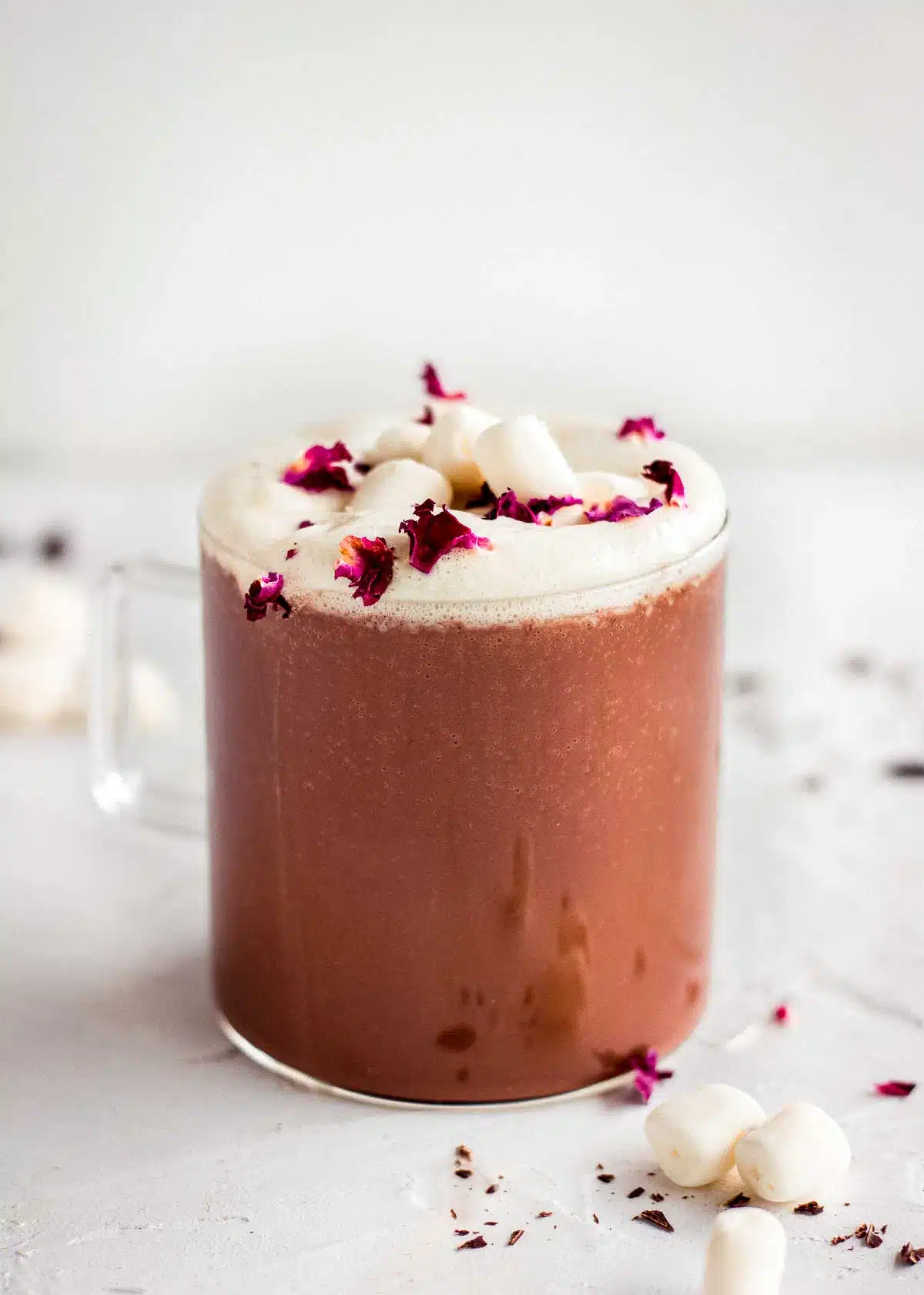 Glass mug of rose hot cocoa topped with whipped cream, rose petals and marshmallows.