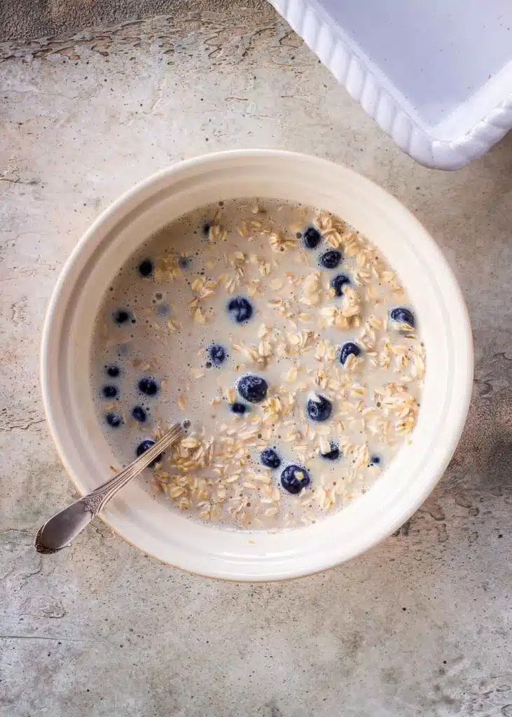A mix of oats, dairy-free milk, blueberries, maple syrup, banana and baking powder in a bowl.