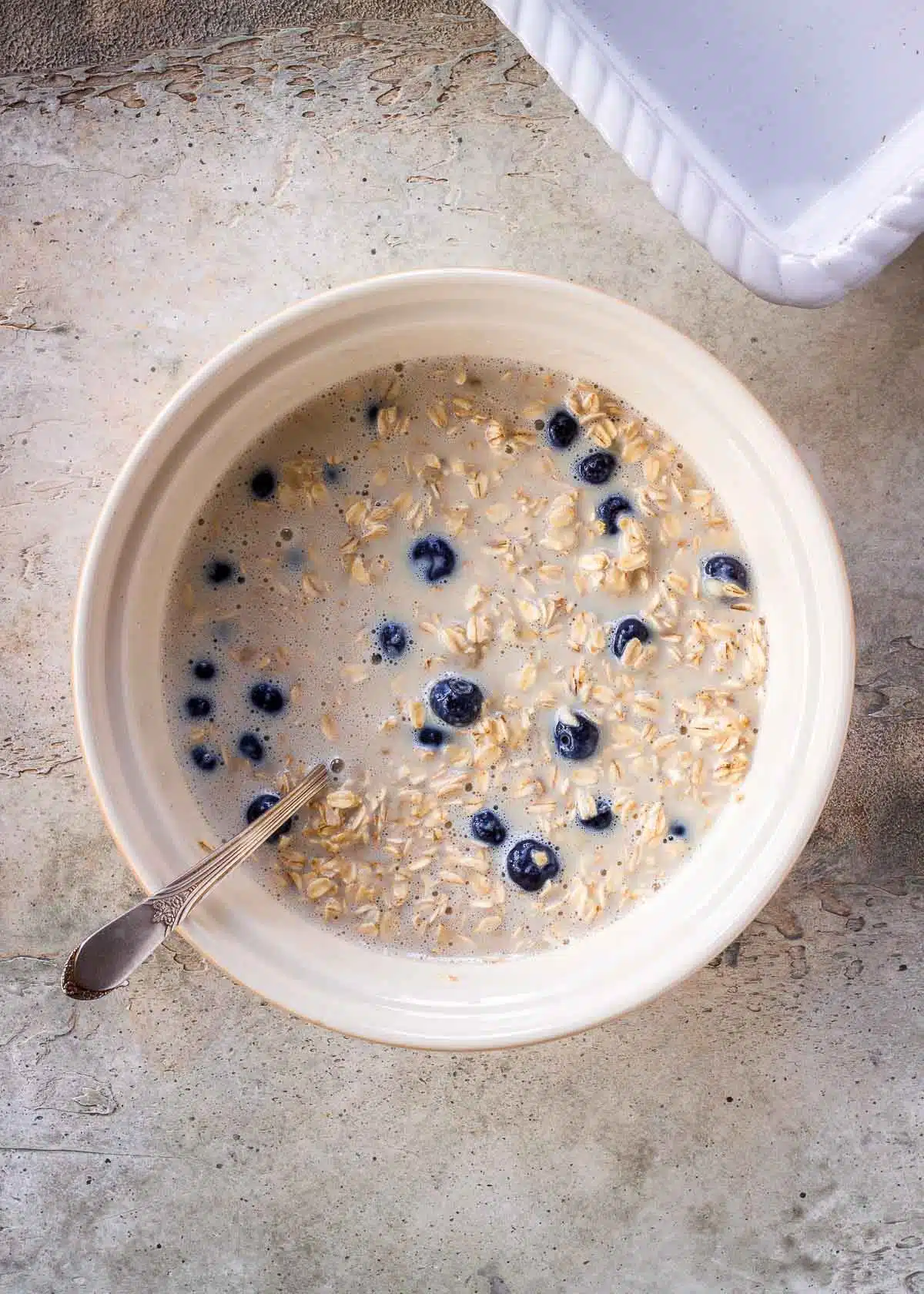 A mix of oats, dairy-free milk, blueberries, maple syrup, banana and baking powder in a bowl.