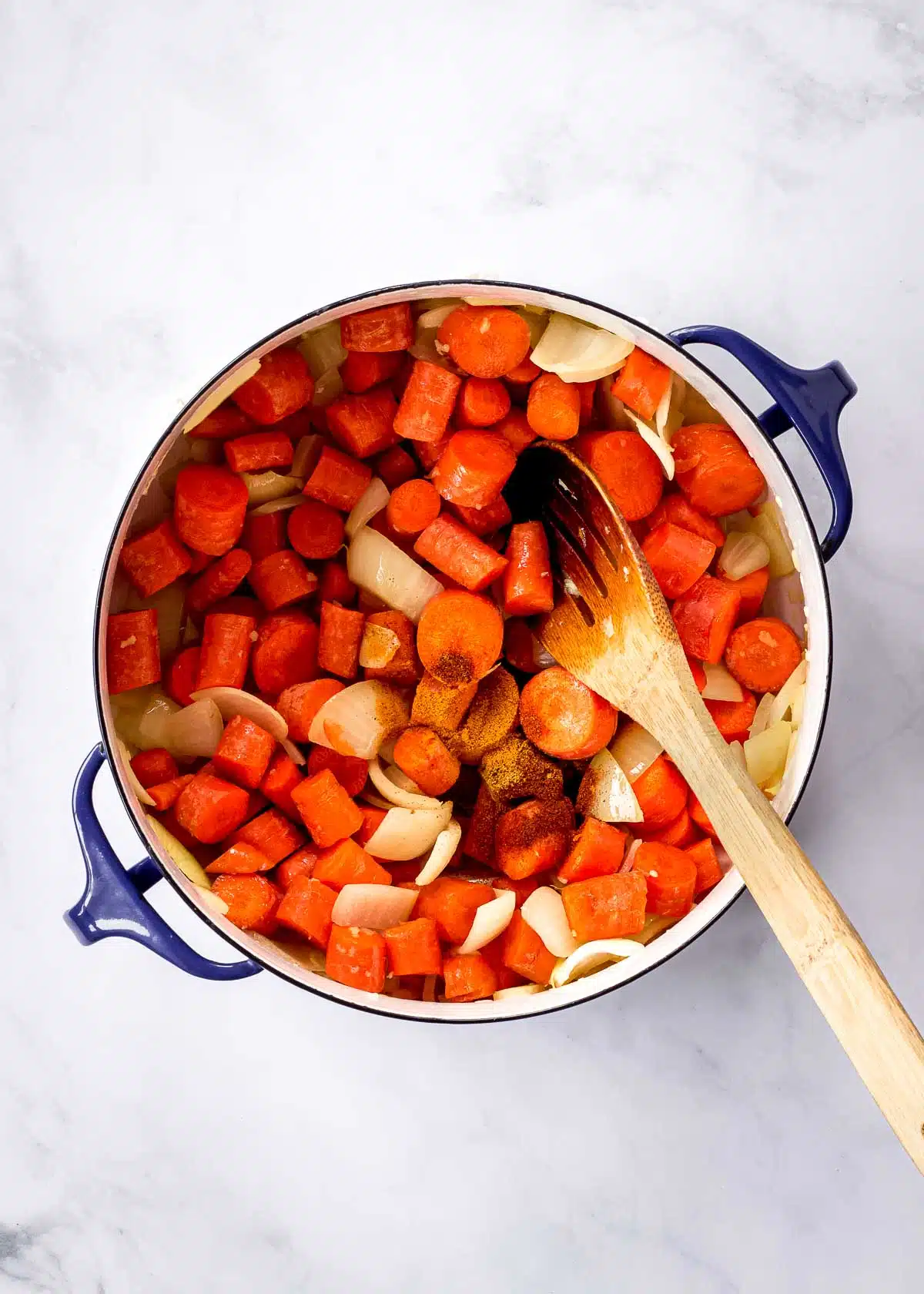 Carrots, onion, garlic and spices in a large pot with a wooden spoon.