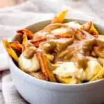 A bowl of vegan poutine made of fries, gravy and cheese curds.