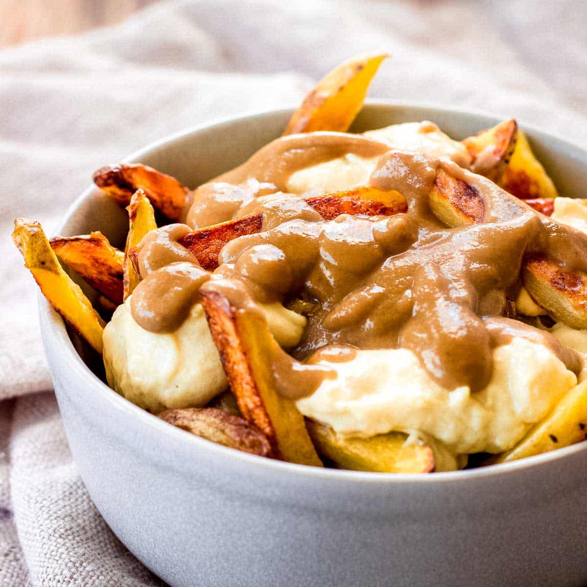 Grey bowl of vegan poutine topped with cheese curds and gravy.