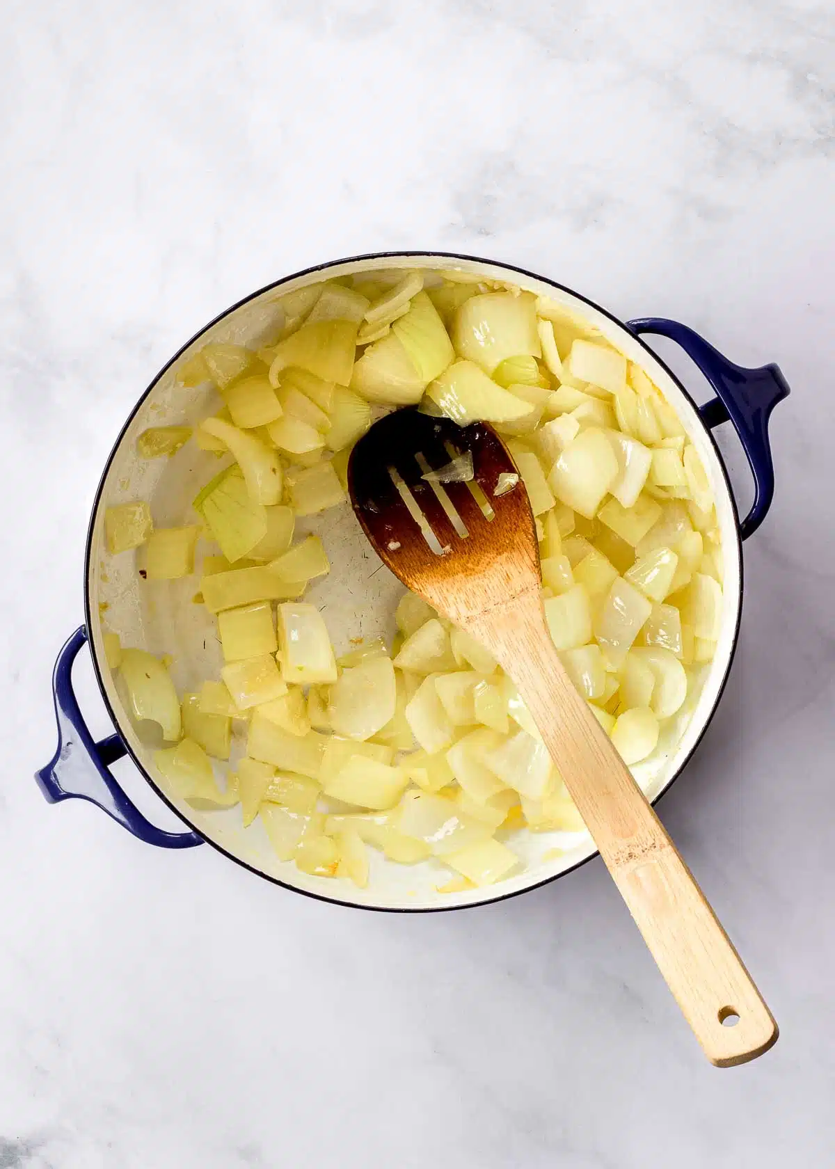 Onion and garlic in a large pot with a wooden spoon.
