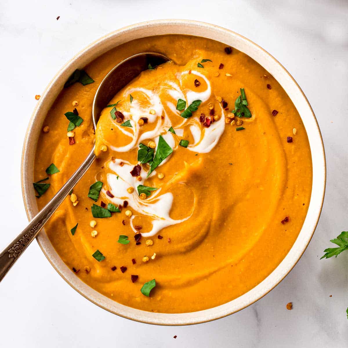 Bowl of lentil carrot soup with a spoon decorated with coconut yoghurt, cilantro and chili flakes. 