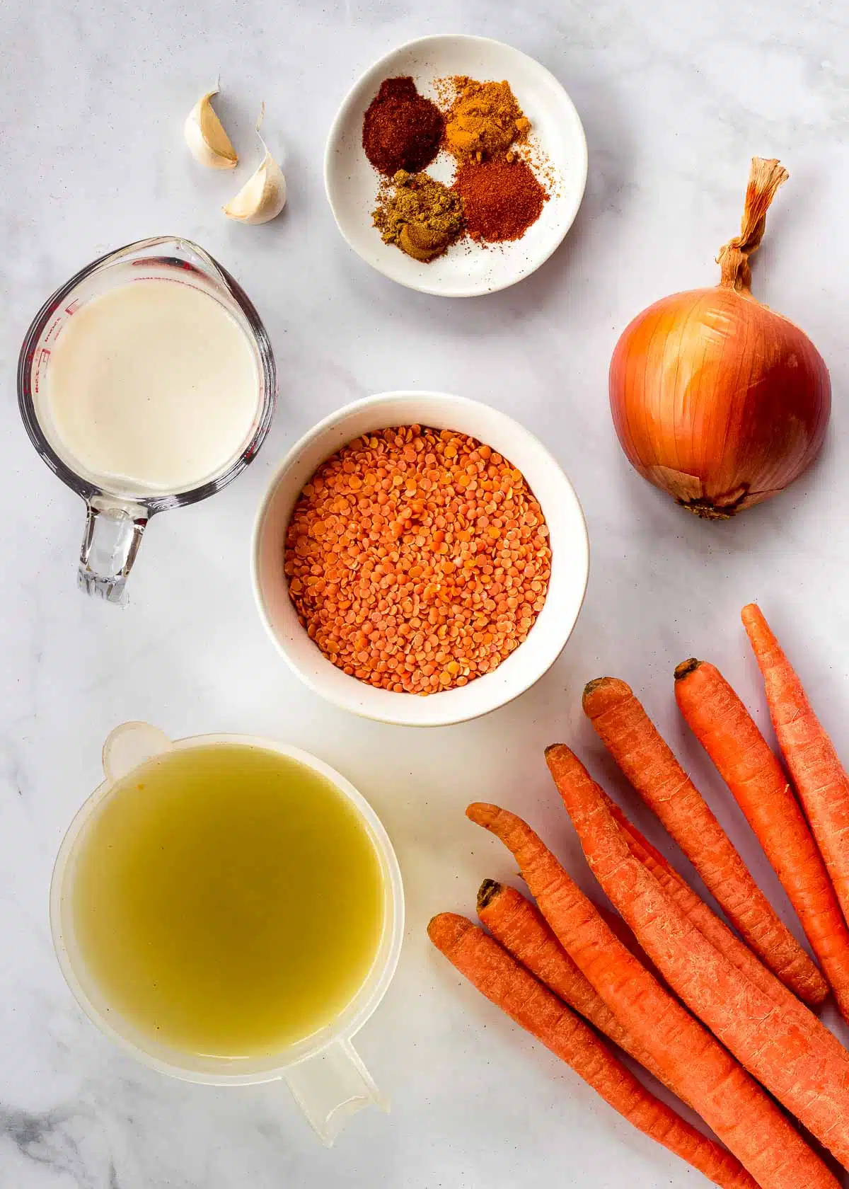 Υλικά για τη σούπα με φακές και καρότο: κόκκινες φακές, κρεμμύδι, σκόρδο, καρότα, ζωμός, μπαχαρικά και γάλα.