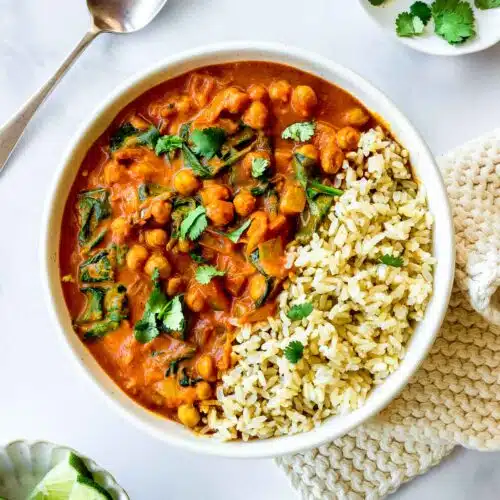 A bowl of Chickpea Spinach Curry and rice decorated with cilantro.