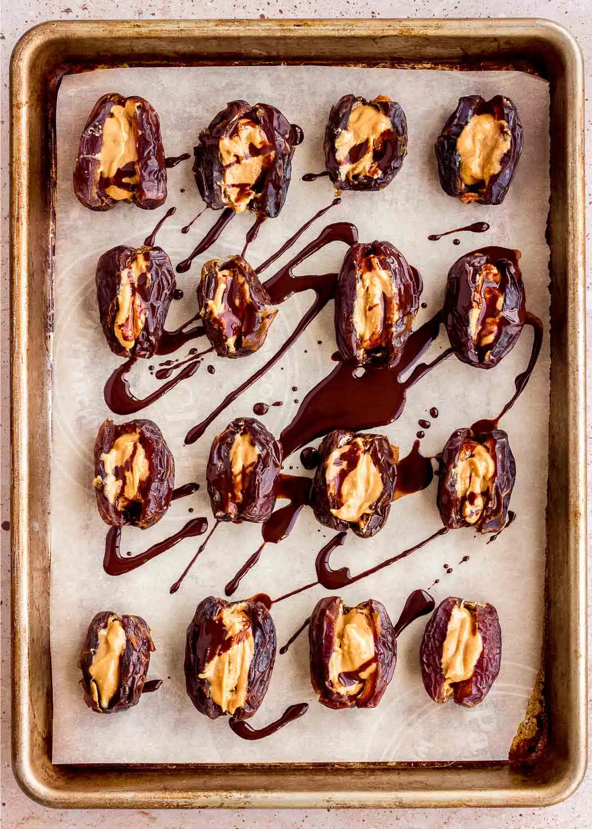 Dates stuffed with peanut butter and drizzled with chocolate on a baking tray.