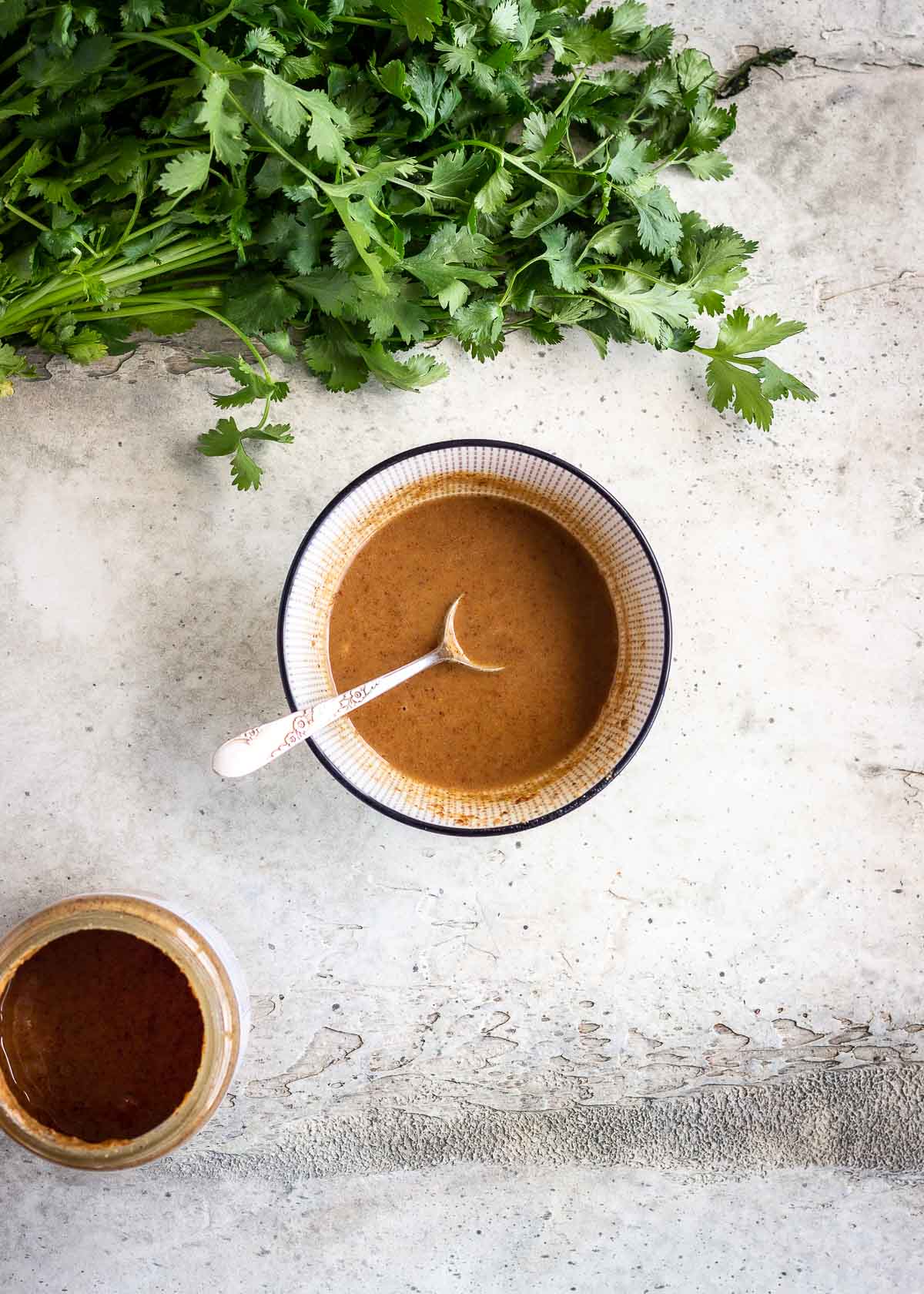 Almond butter sauce in a small bowl with a spoon, with some cilantro nearby.