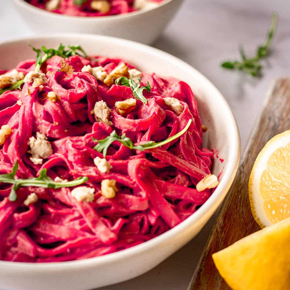 White bowl of beet pasta sauce with arugula and lemons by Elizabeth Emery of Vancouver with Love.