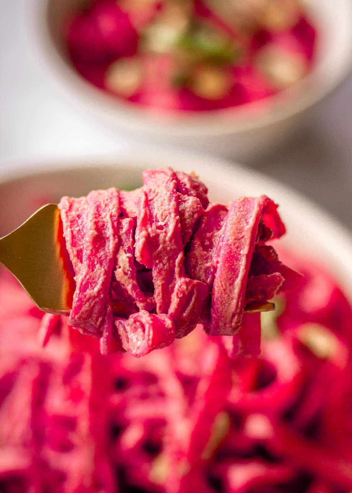 Closeup of a forkful of pasta in a pink beetroot sauce.