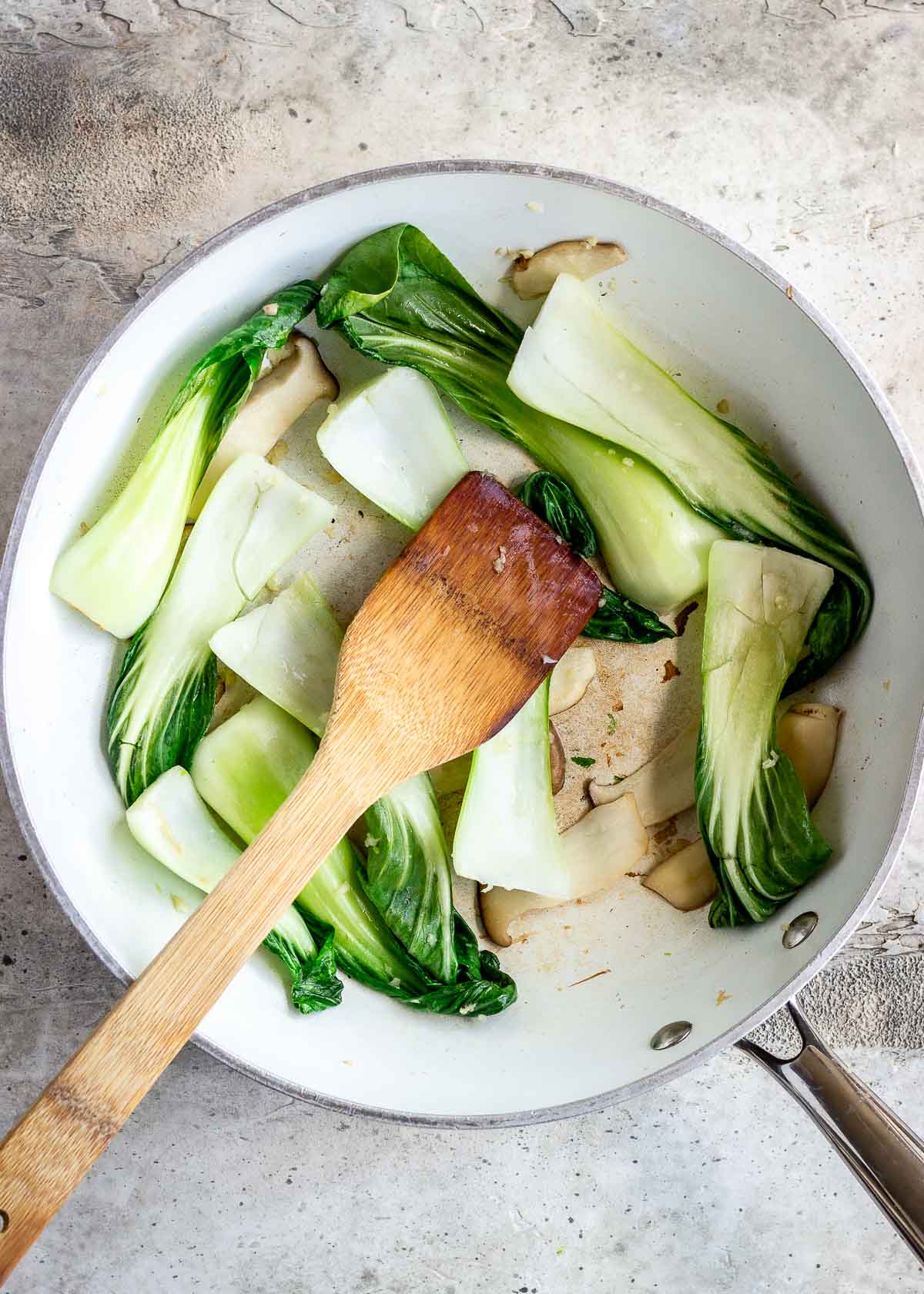 Bok choy and mushrooms being cooked together in a white wok.