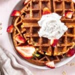 3 Ingredient Oatmeal Waffles on a plate decorated with strawberries and coconut whipped cream.