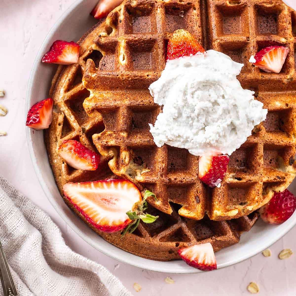 Plate of oatmeal waffles with coconut whipped cream and strawberries.