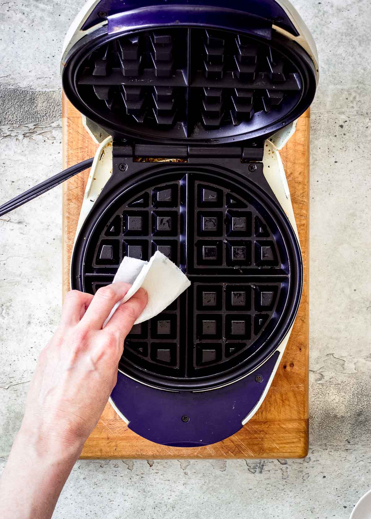 A woman's hand greasing a waffle iron with coconut oil on kitchen paper.