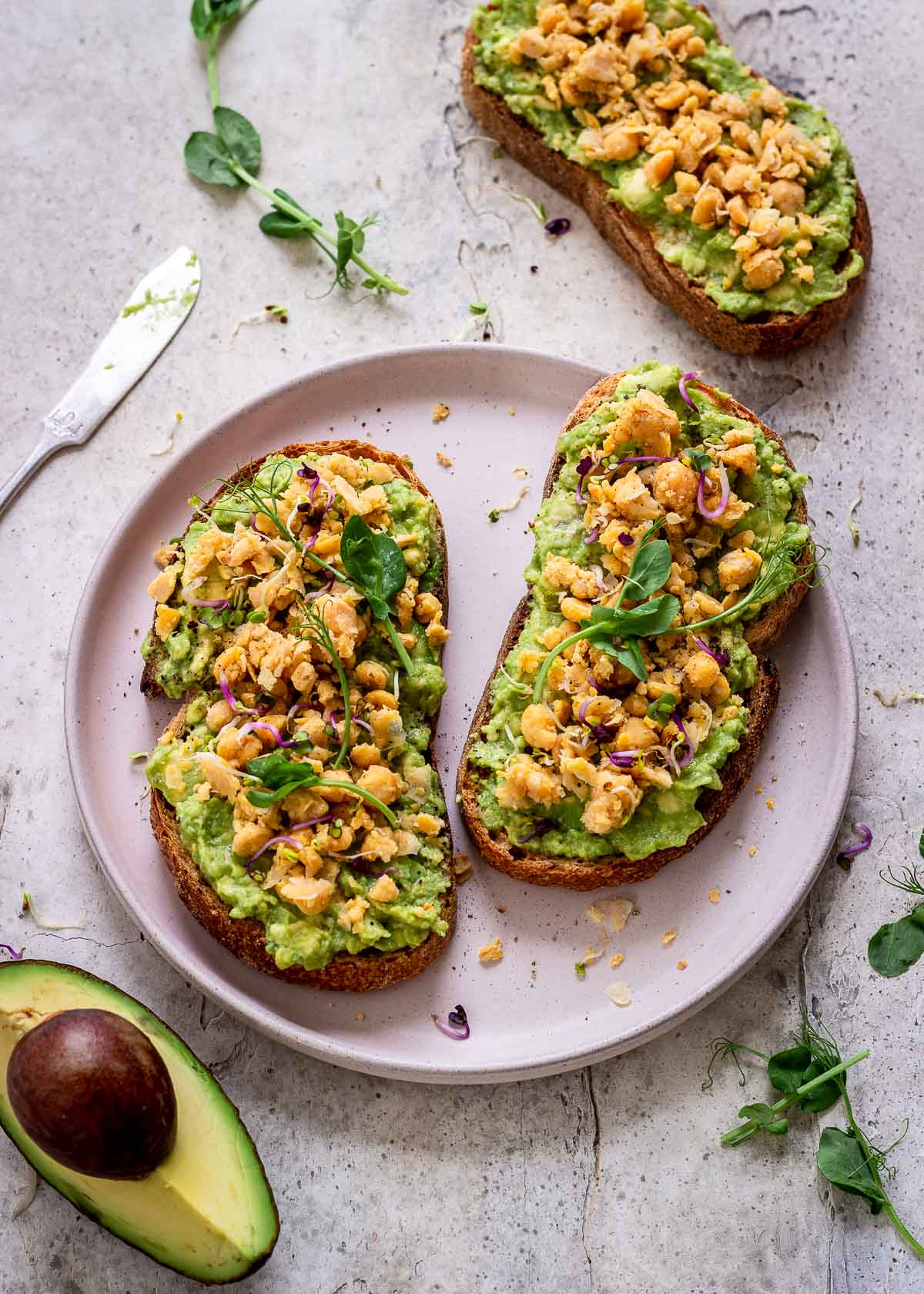 High protein vegan avocado toast on a pink plate with chickpeas, pea shoots and sprouts.