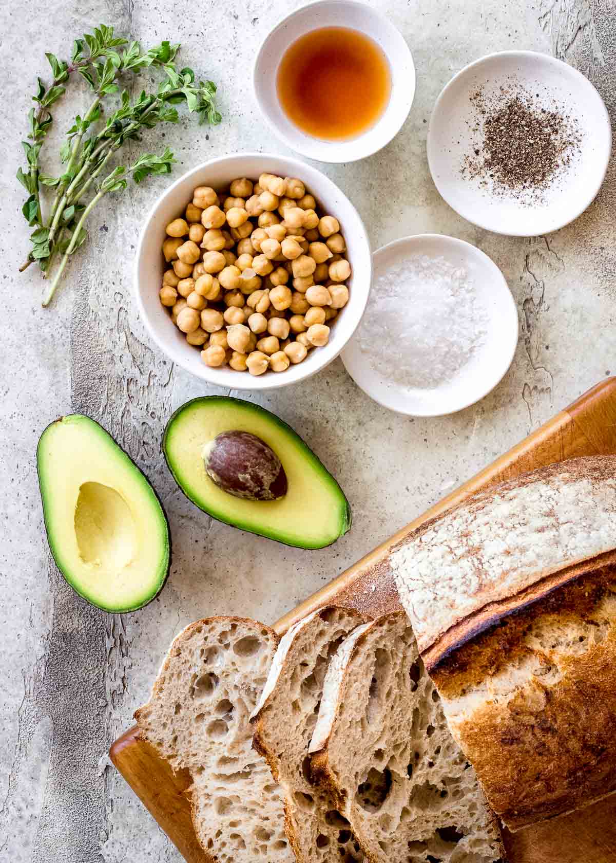 Ingredients for high protein vegan avocado toast, including sourdough bread, avocado, chickpeas and herbs.