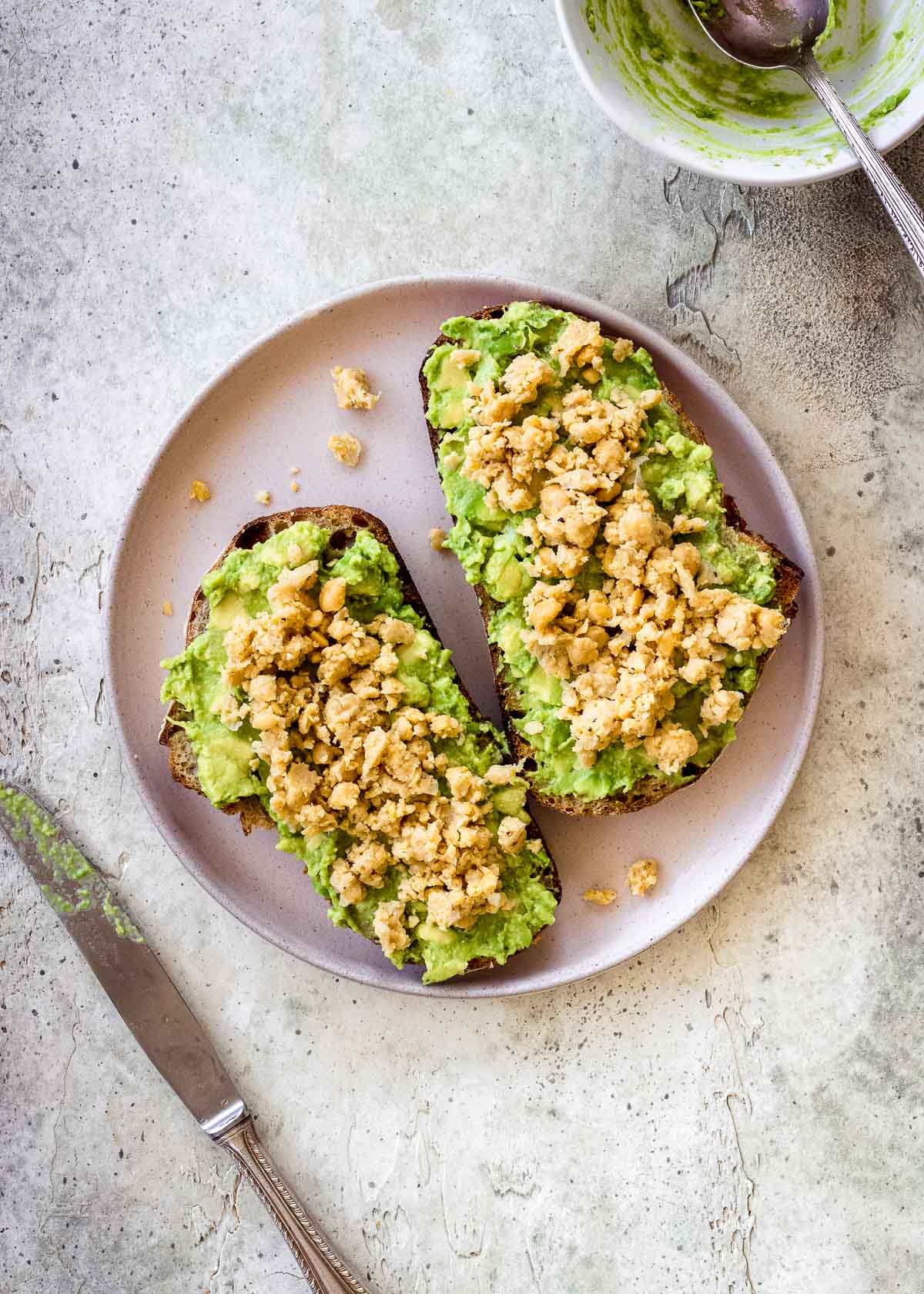 High protein vegan avocado toast with chickpeas on a pink plate.