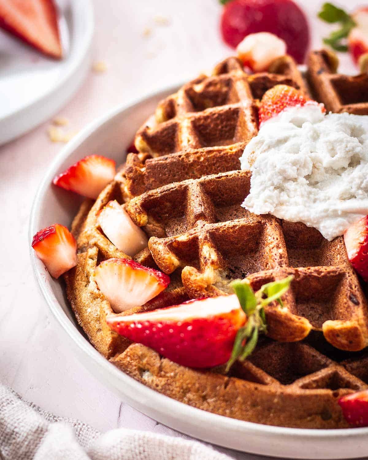 Vegan Oat Waffles on a plate decorated with strawberries and coconut whipped cream.