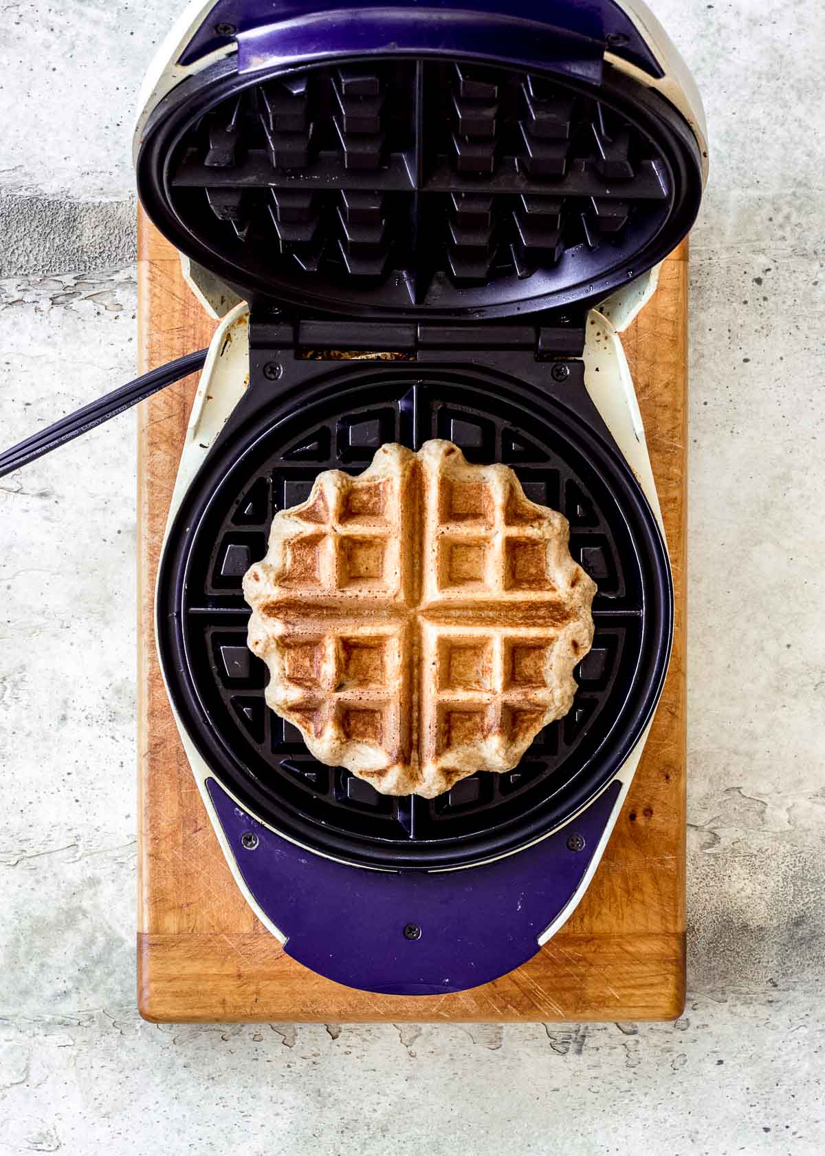 Cooked vegan waffle sits in a waffle iron, ready to be removed.