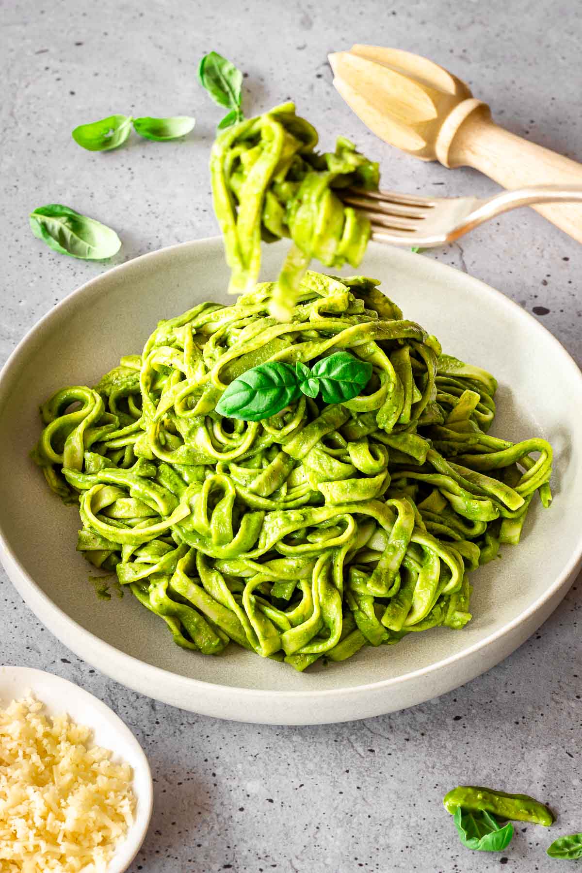 Grey plate of creamy spinach pasta sauce on fettuccine. Dish is decorated with basil leaves and there is a fork of pasta in the foreground.