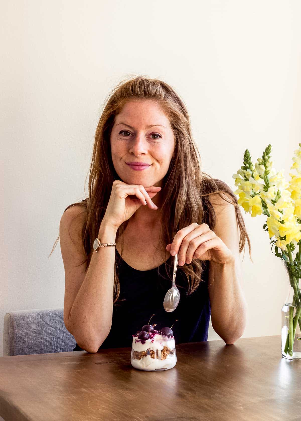 Elizabeth Emery smiling at camera whilst eating a vegan parfait.