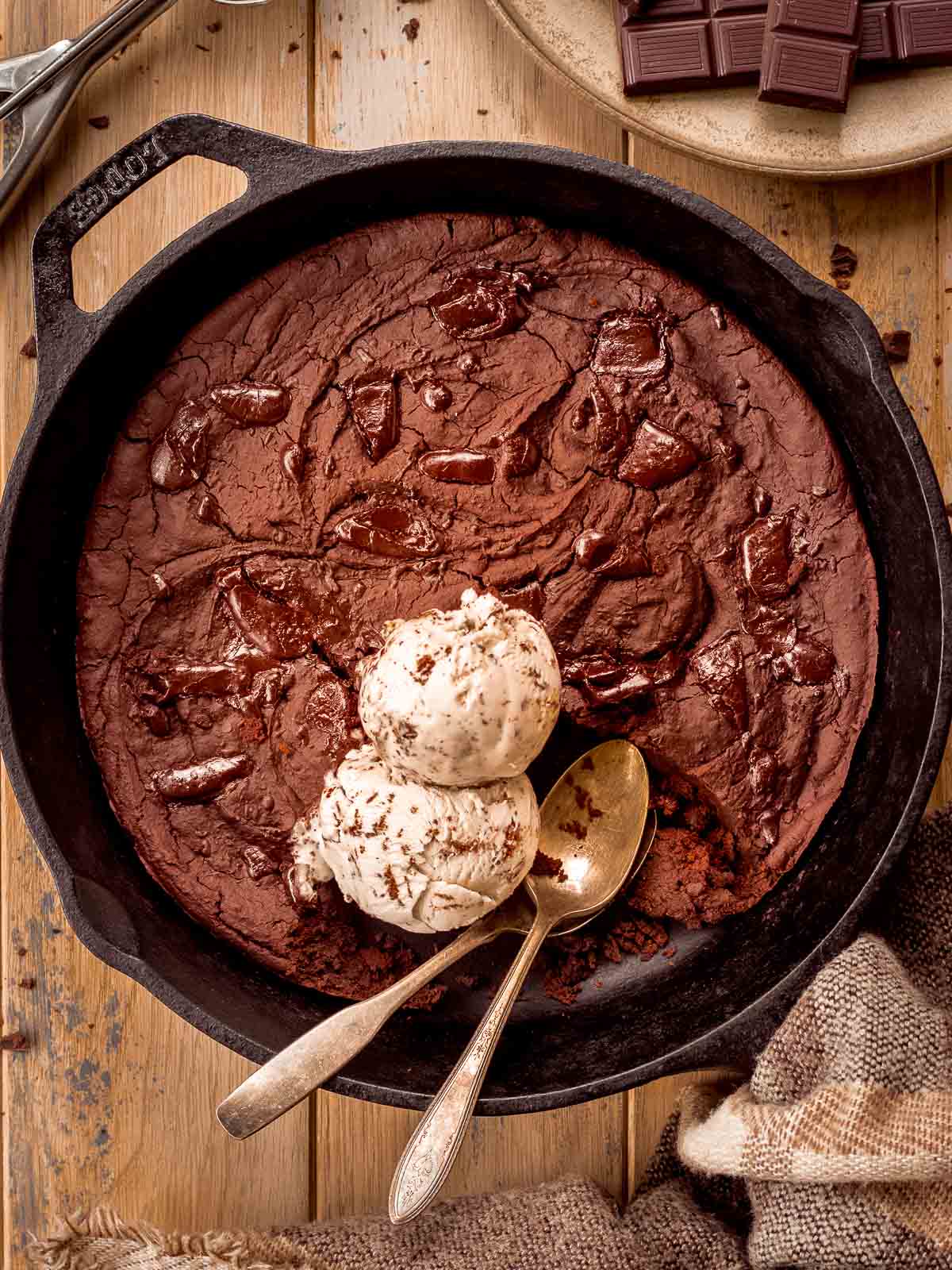 Brownie skillet with chocolate chips. Two scoops of ice cream are mixed into the skillet with two spoons.